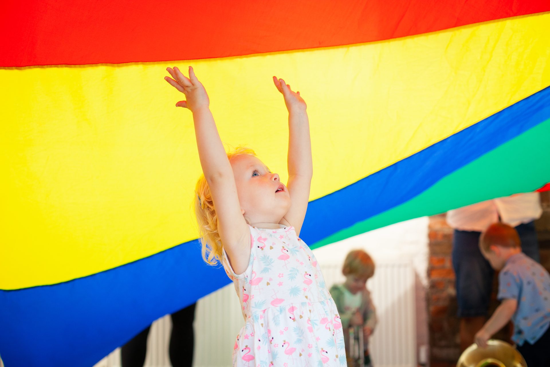 Little girl with hands in the air underneath a play parachute at a Mini Mozart music class for babies and toddlers