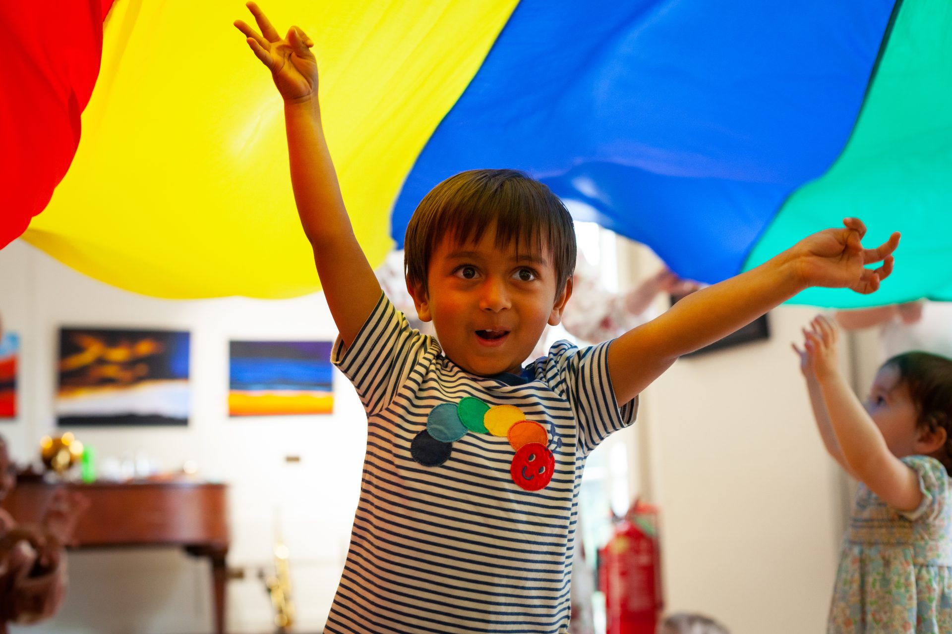 Toddler dancing underneath play parachute at a Mini Mozart Music Class for toddlers